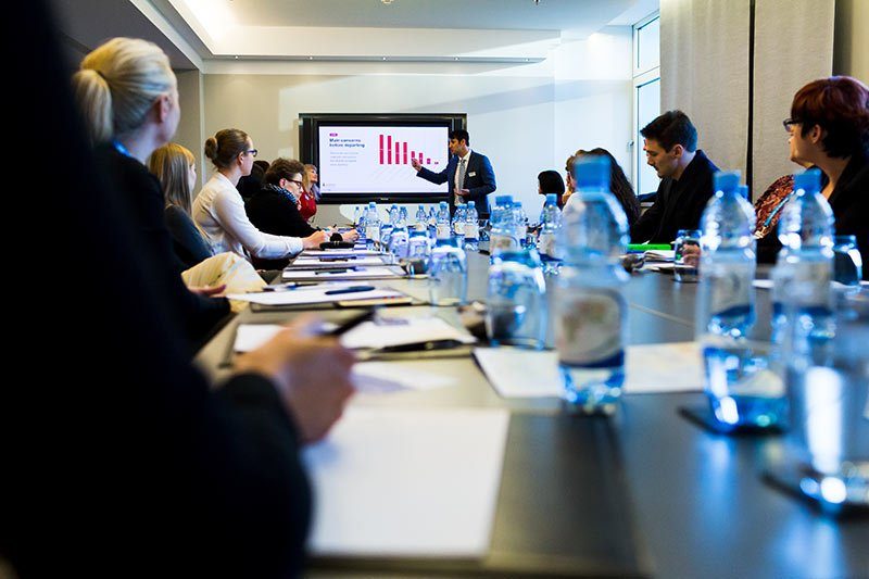 Ein Redner pr&auml;sentiert bei einem Business-Meeting in Berlin, umgeben von konzentrierten Teilnehmern.