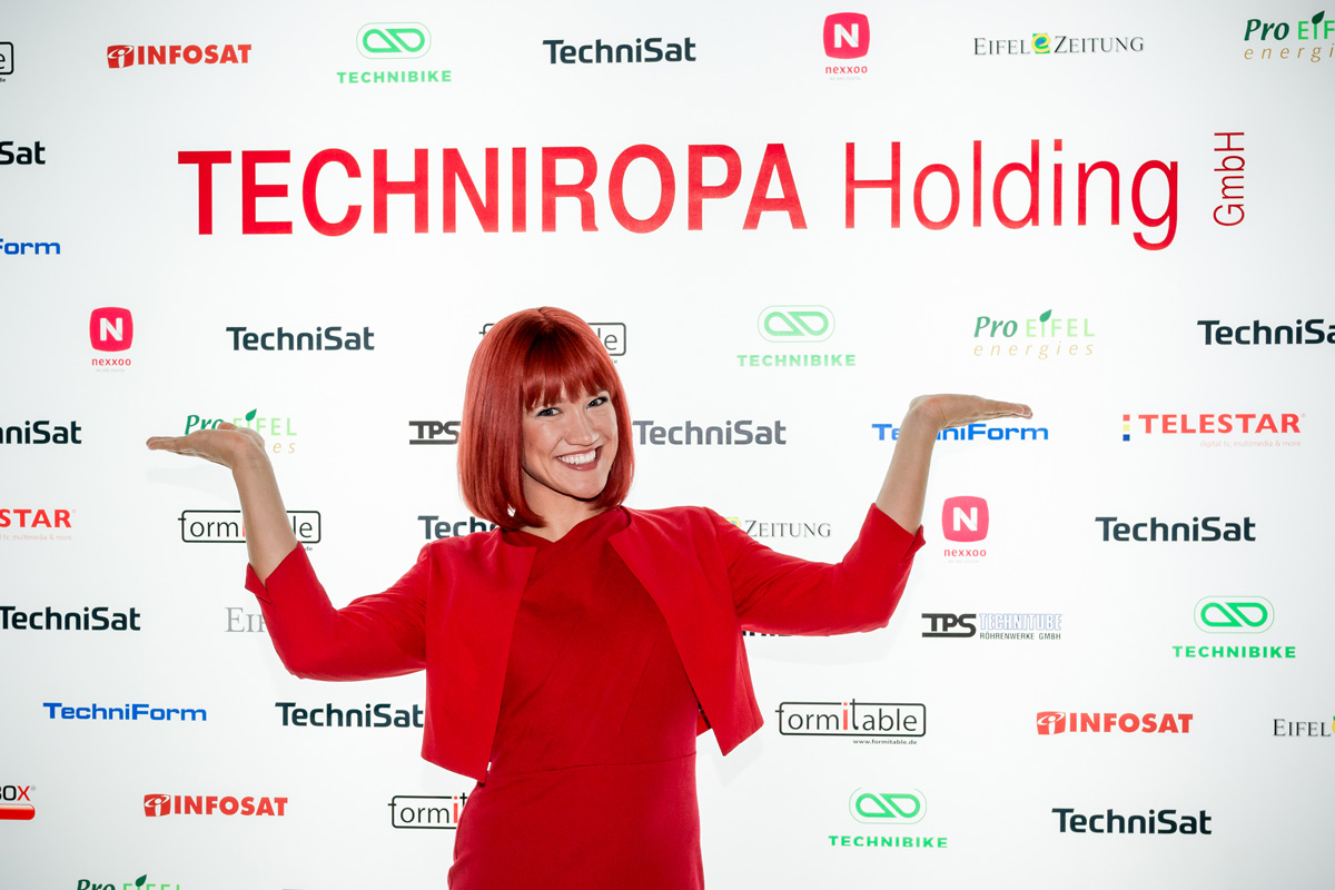 Miss IFA 2018 Nadine präsentiert die TechniRopa Holding vor einer Fotowand auf der IFA 2018.