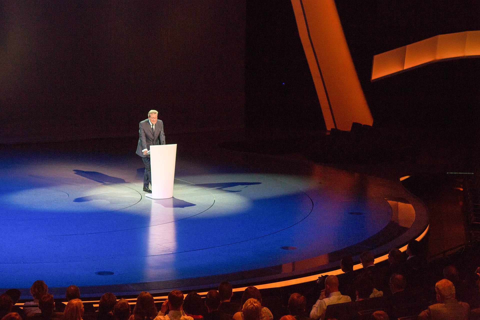Eventfotograf Berlin und Kongressfotograf Berlin bei der Arbeit: Ein Redner steht an einem Podium auf einer gut beleuchteten B&uuml;hne w&auml;hrend eines Kongresses in Berlin.
