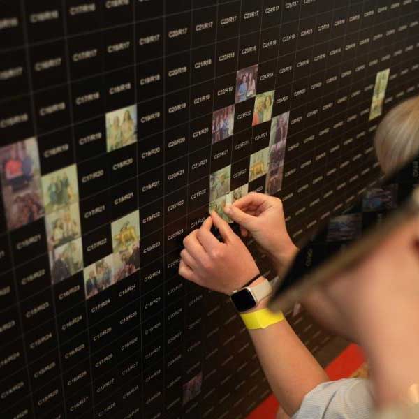 Nahaufnahme von Händen, die ein Foto an eine schwarze Rasterwand anbringen.