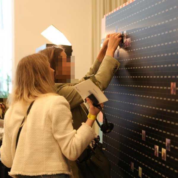 Gäste interagieren mit der Fotomosaic Wall, indem sie Fotos auf die schwarze Rasterfläche kleben.